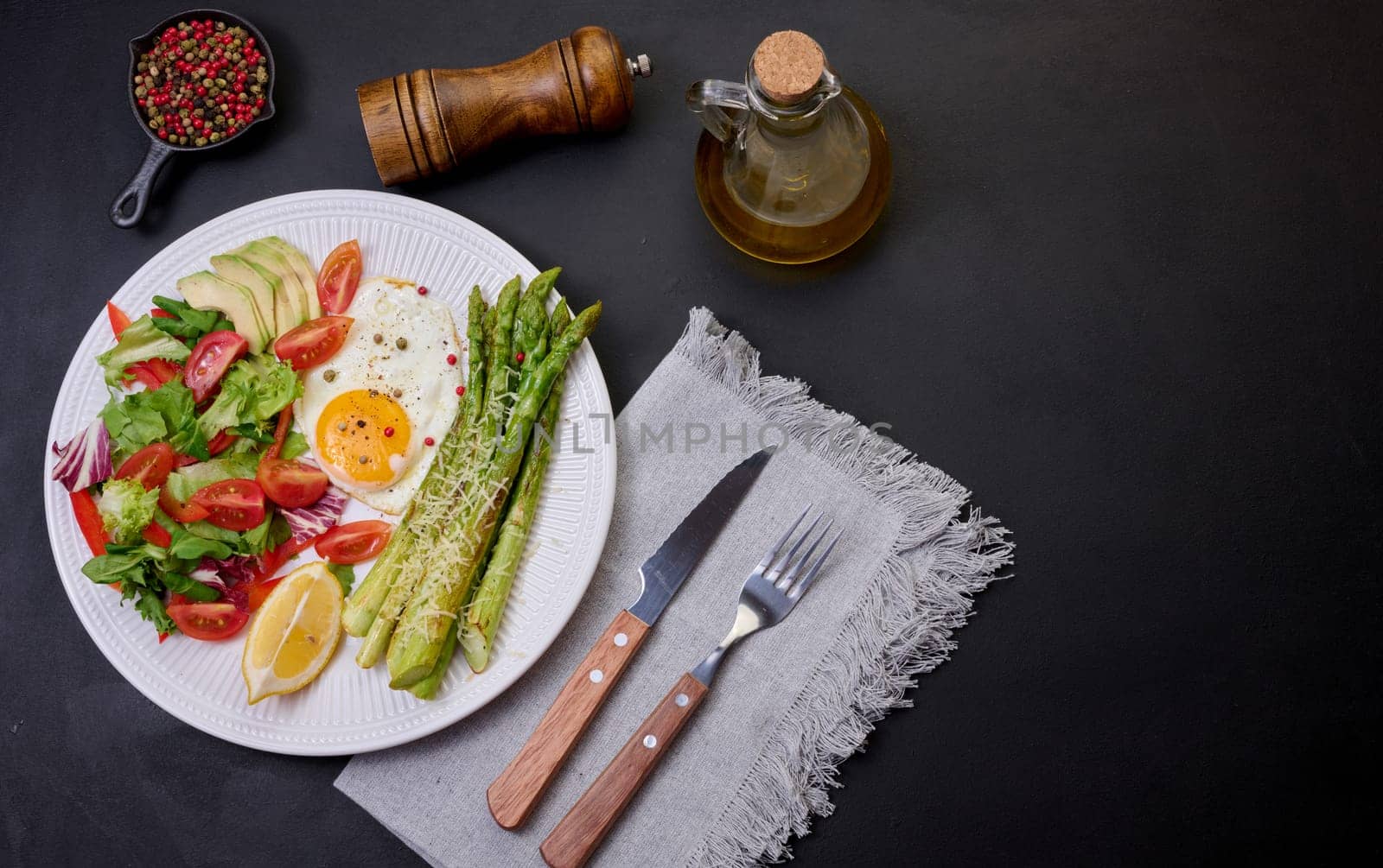 Round plate with cooked asparagus, fried egg, avocado and fresh vegetable salad on the table, top view