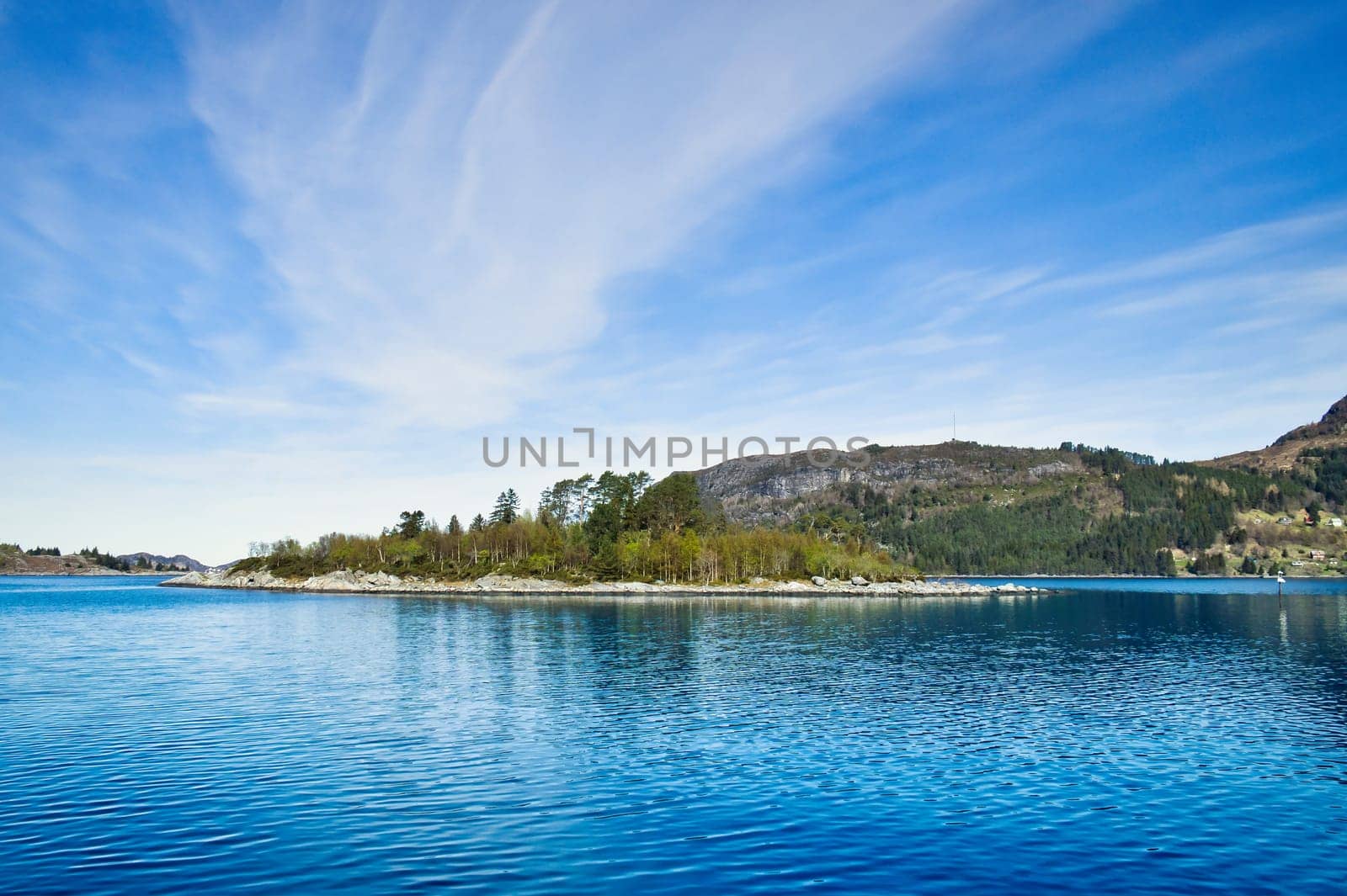 Island with rocks and trees in the fjord in front of the open sea in Norway. The water glistens in the sun. Landscape from the north