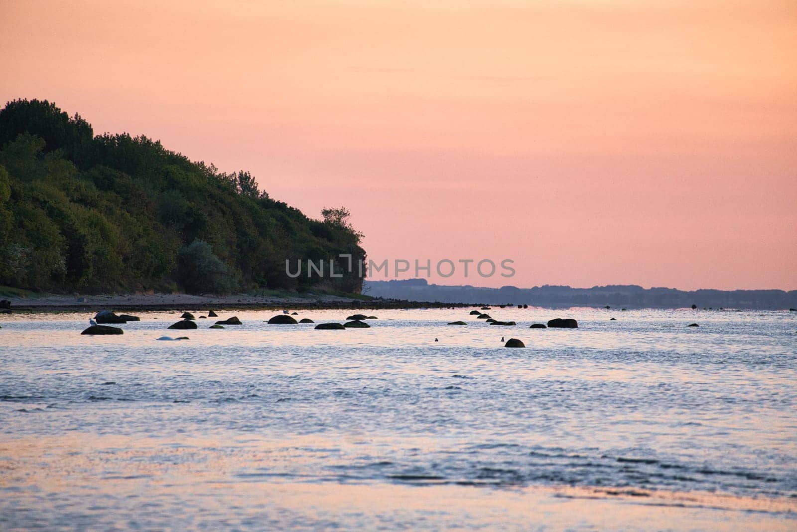 Sunset, illuminated sea. Sandy beach in the foreground. Light waves. Poel island on the Baltic Sea. Nature photo from the coast