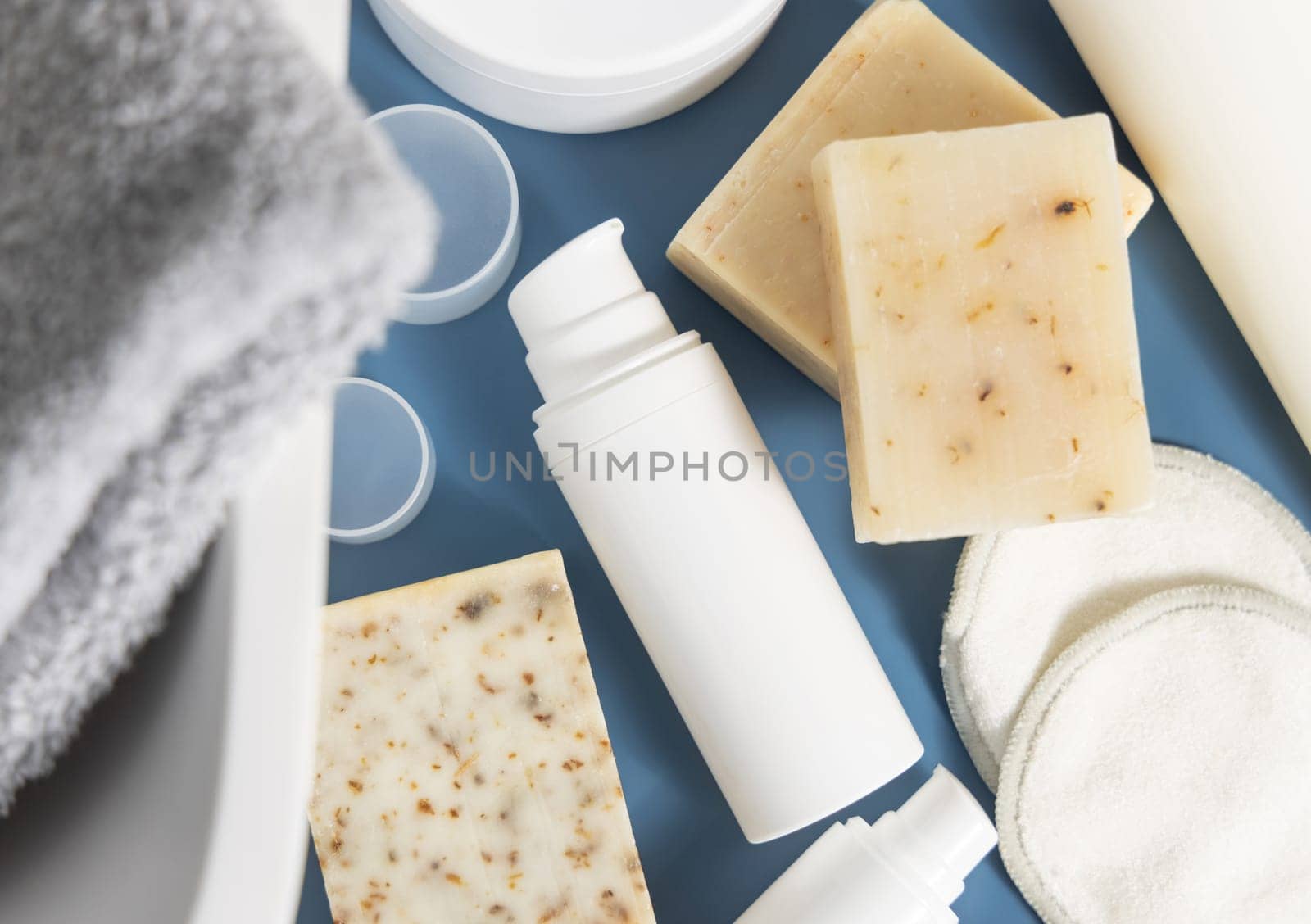 White one pump cosmetic bottle near soap bars and basin on blue countertop in bathroom top view, mockup. Modern lifestile scene with female personal care and beauty products