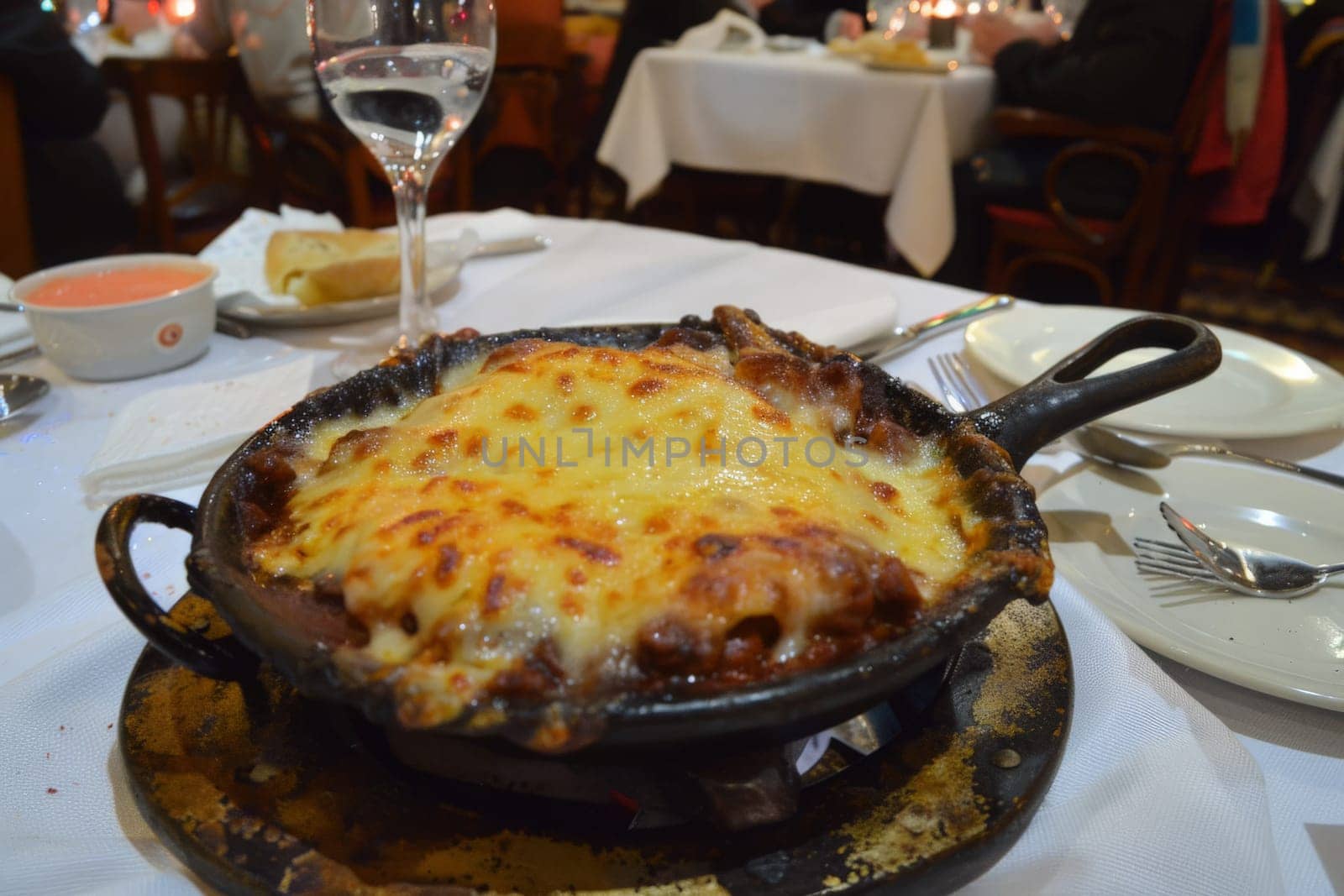 A piping hot skillet of golden-brown, cheese-covered enchiladas at a lively dinner setting.