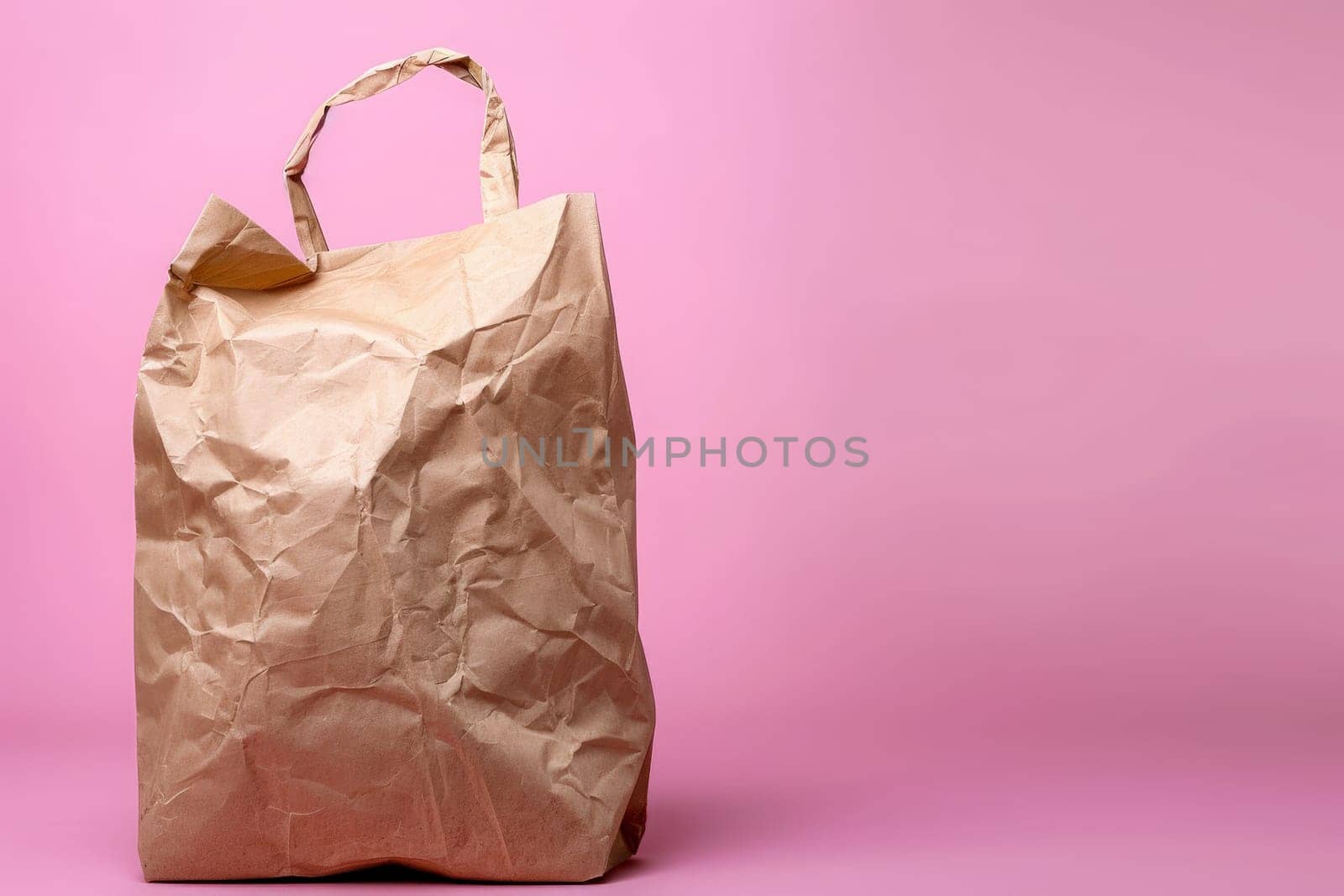 A solitary wrinkled paper bag evokes a minimalist vibe on pink.