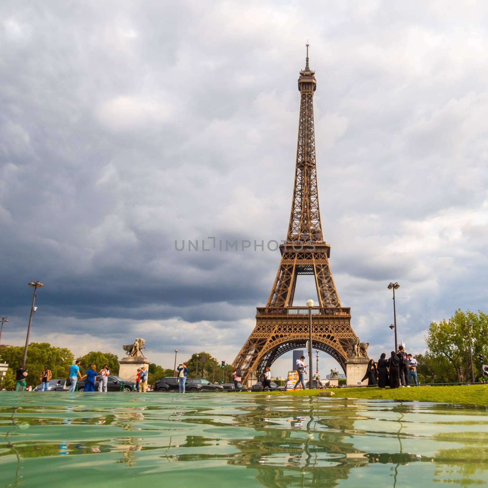 Paris, France - August 29 2023: Tourists and Eiffel tower seen from Trocadero Fountains in a cloudy day. Squared photography taken in Paris.