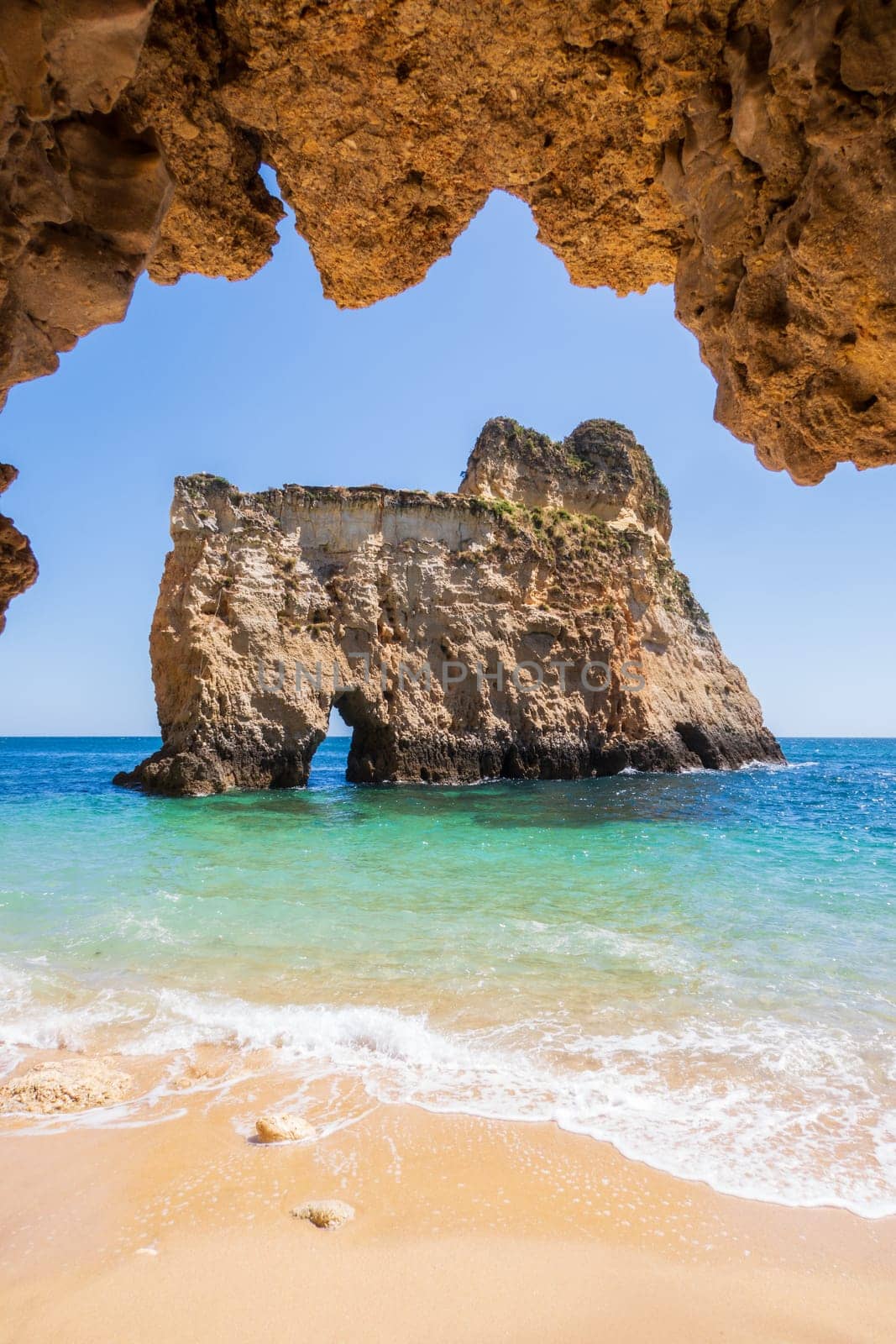 Small, heavenly and difficult to access beach vertically photographed from inside a cave, near Portimão in the Algarve region of Portugal