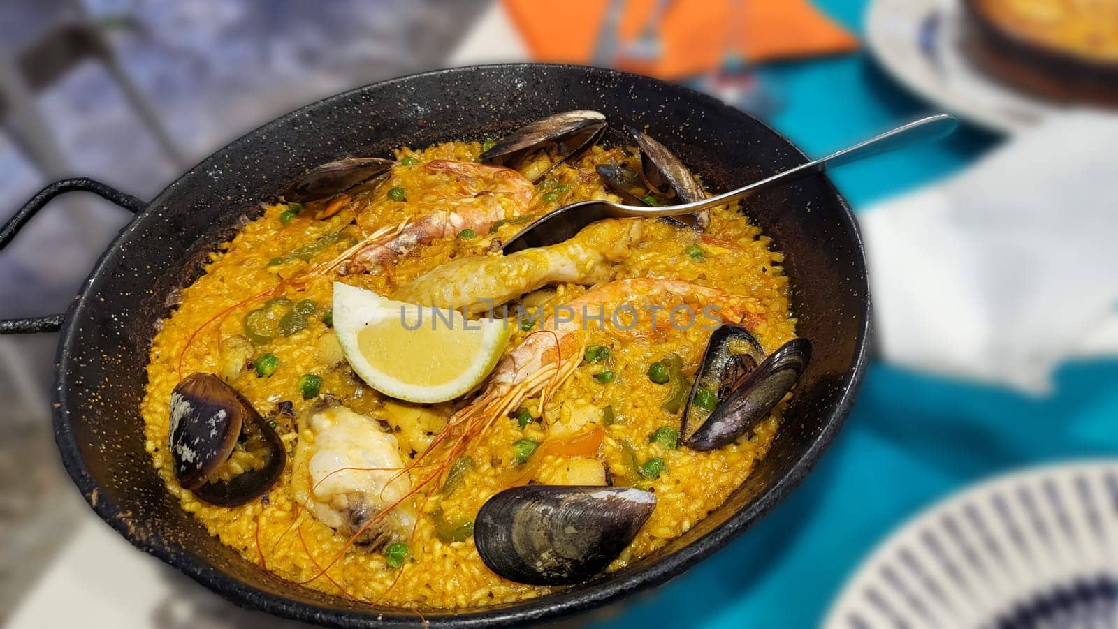Classic dish of Spain, seafood paella in traditional pan on white wooden background top view. Spanish paella with shrimps, clamps, mussels, green peas, fresh lemon wedges from above, space for text