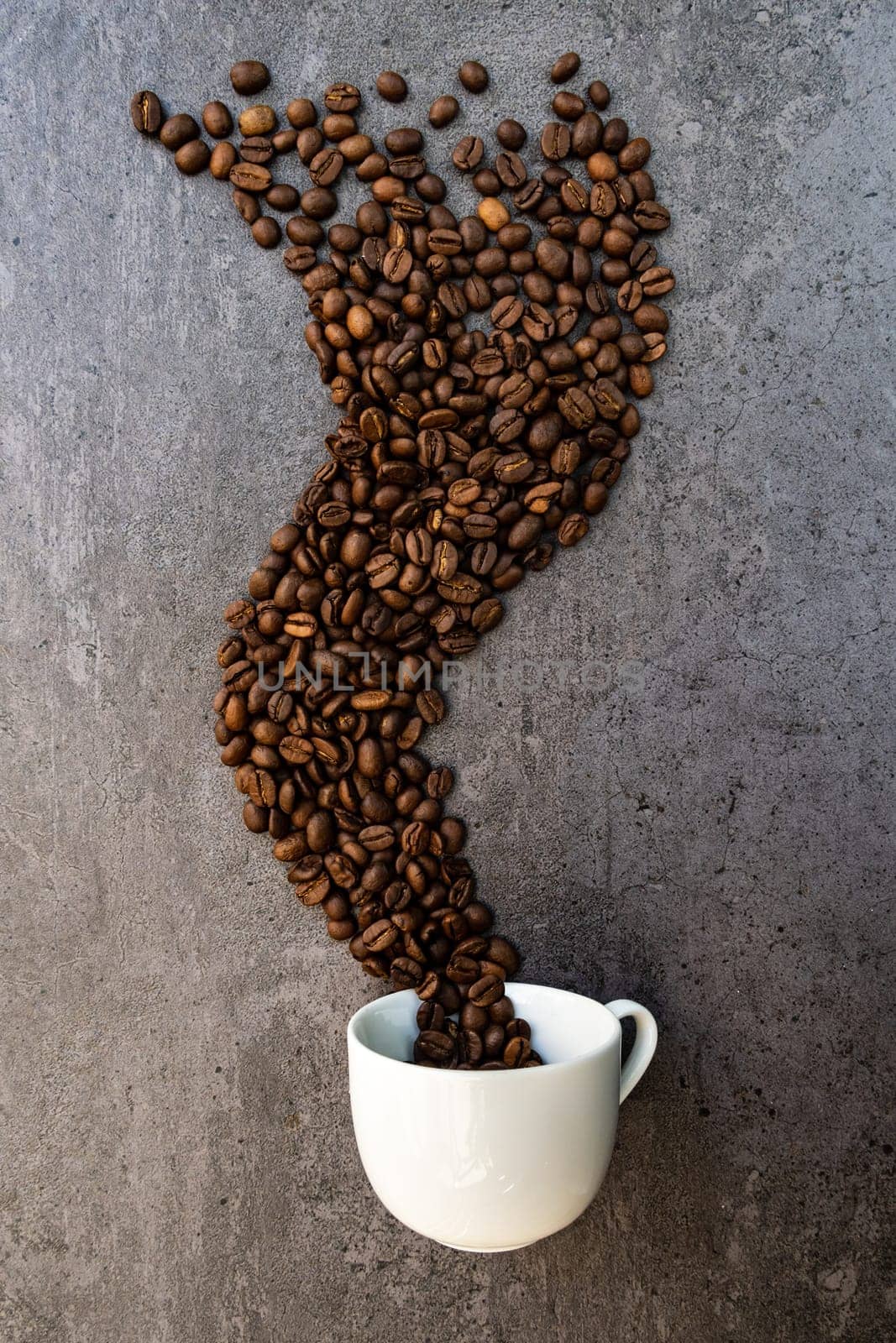 Spilled cup of coffee with roasted  beans forming like a smoke shape, vertical