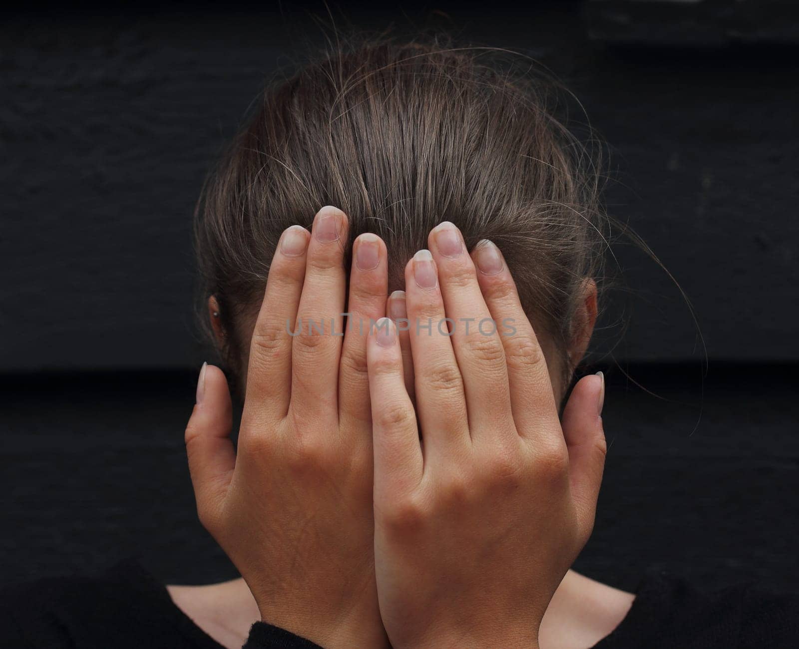 beautiful woman covering her face with her hands against black background