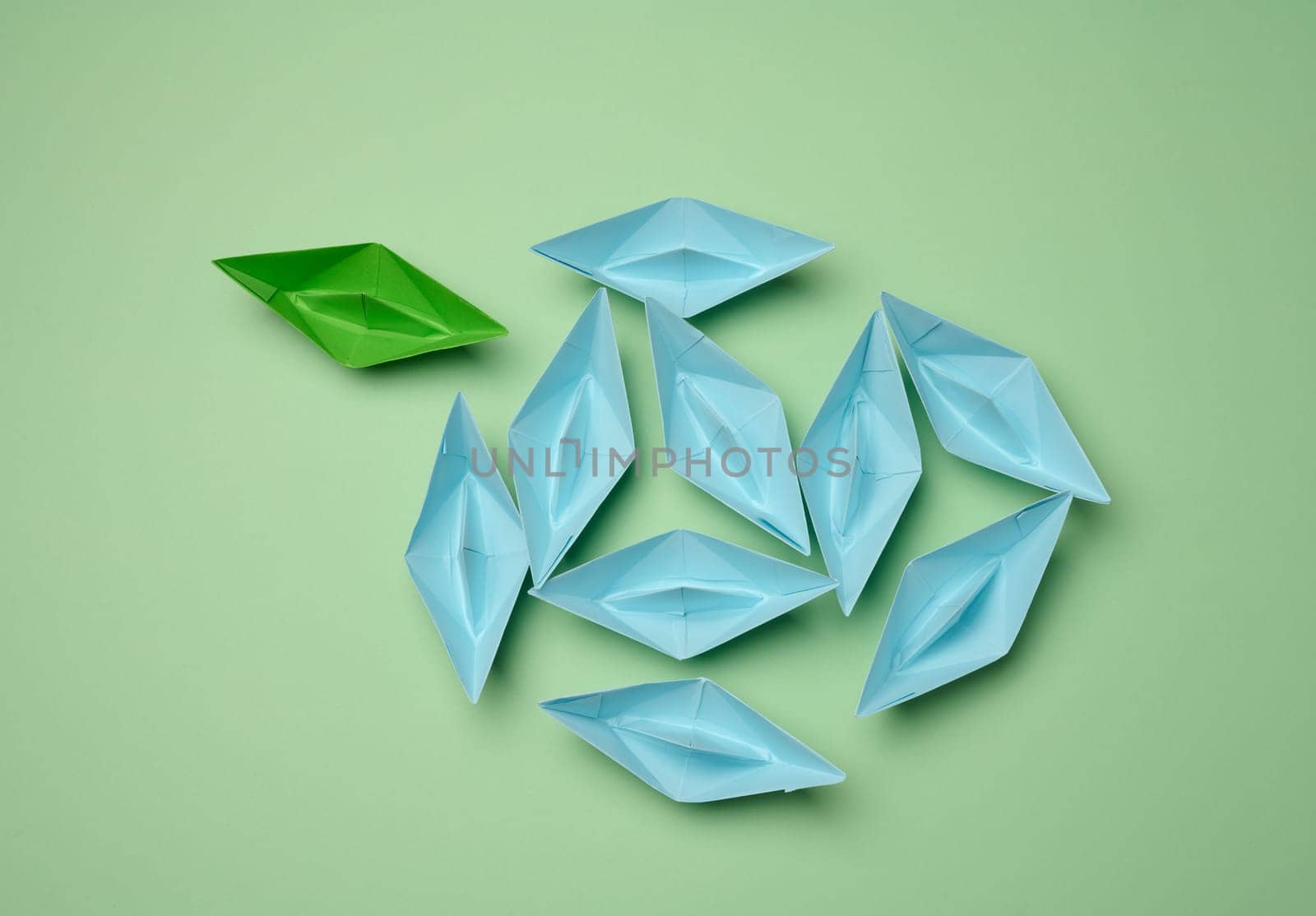 Group of blue paper boats heading in one direction and one green one heading in the opposite direction. The concept of individuality, uniqueness and talent of the employee. Get away from the influence