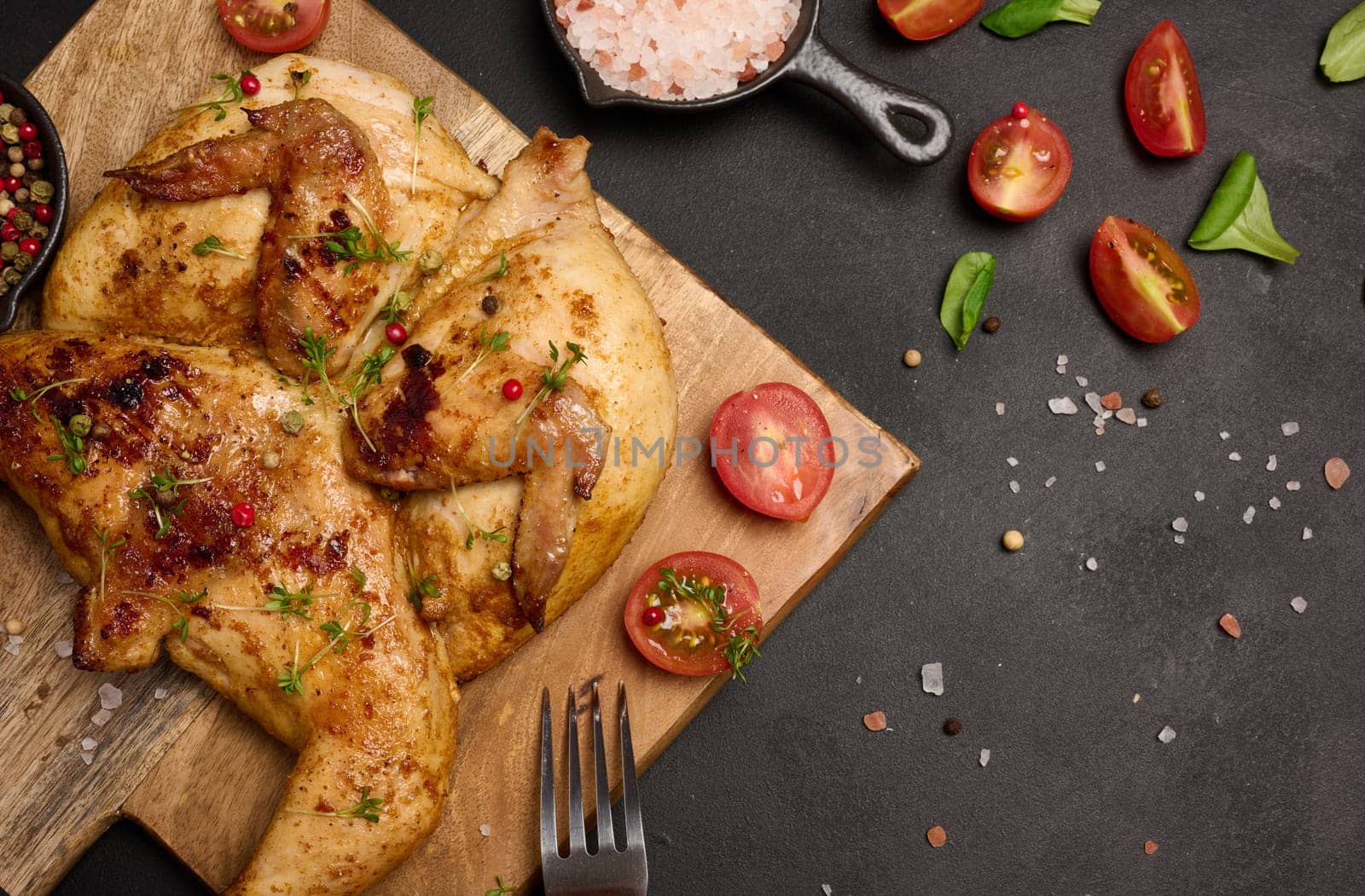 Whole fried chicken with spices on a wooden board on a black table, top view