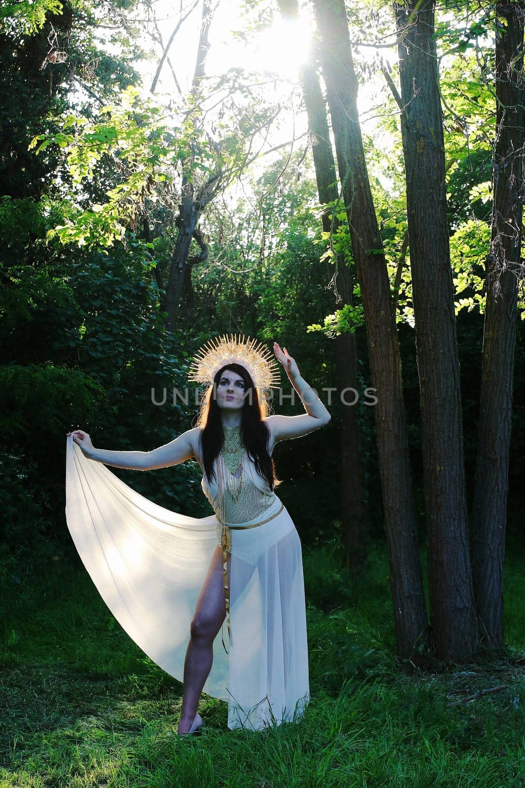 A woman as a goddess stands in the forest, backlit by the sun