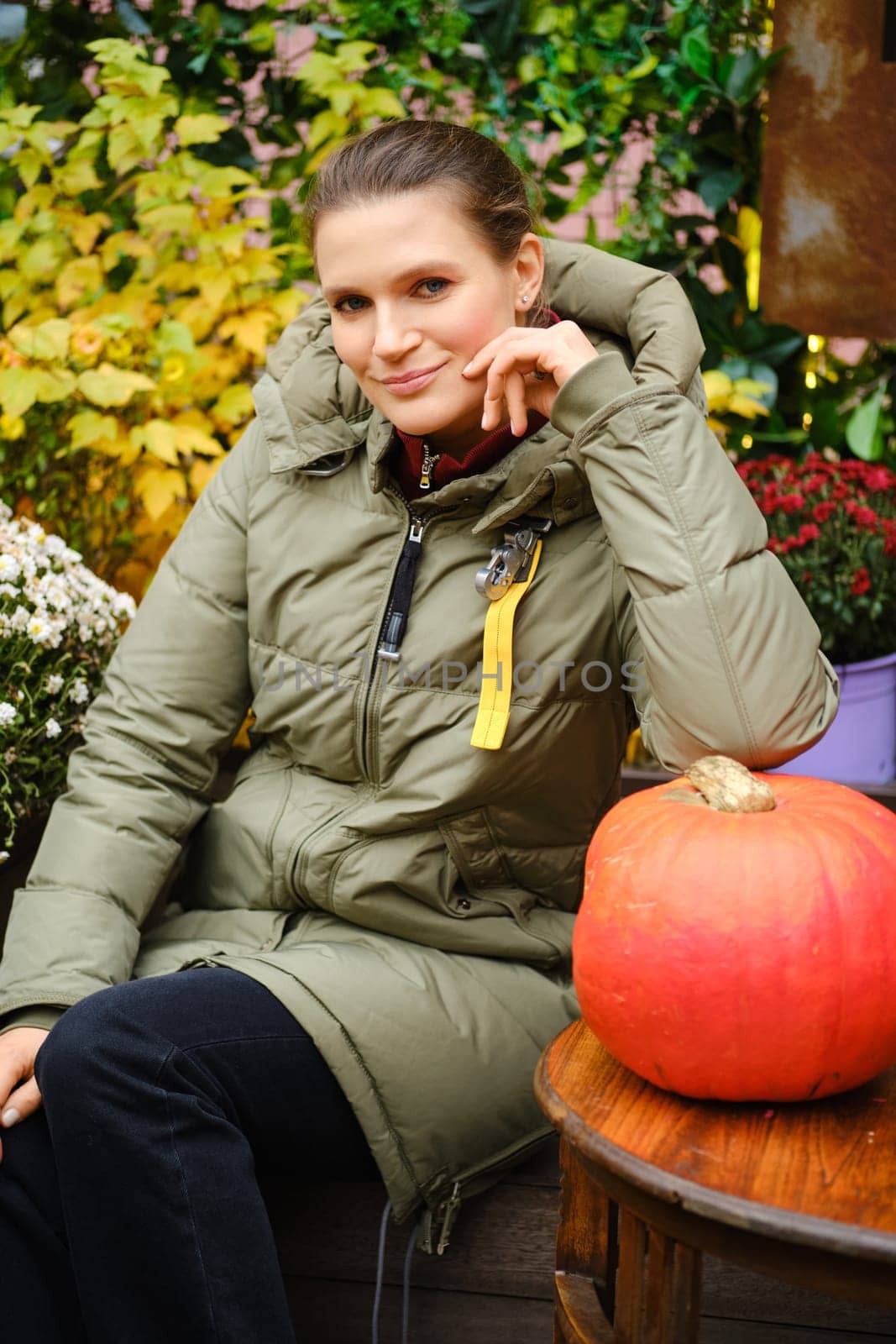 Smiling mid-aged woman in warm down jacket among autumn decoration