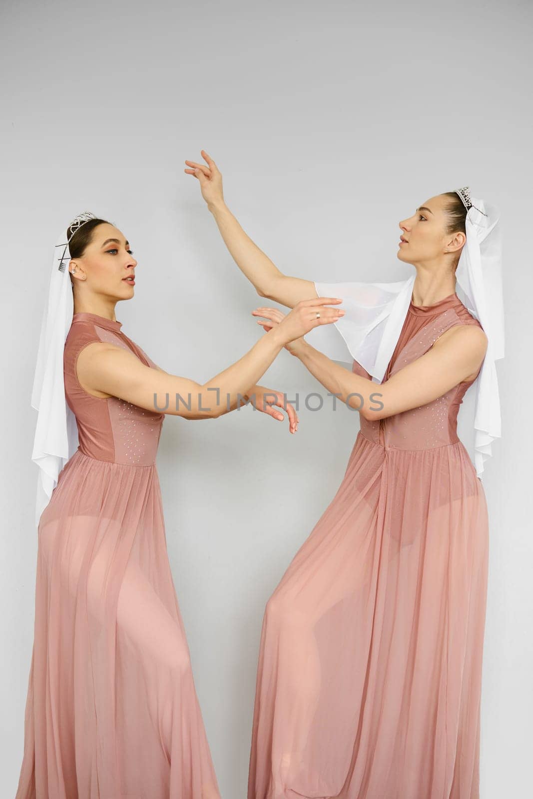 Two beautiful ballerinas practicing in front of each other over grey wall