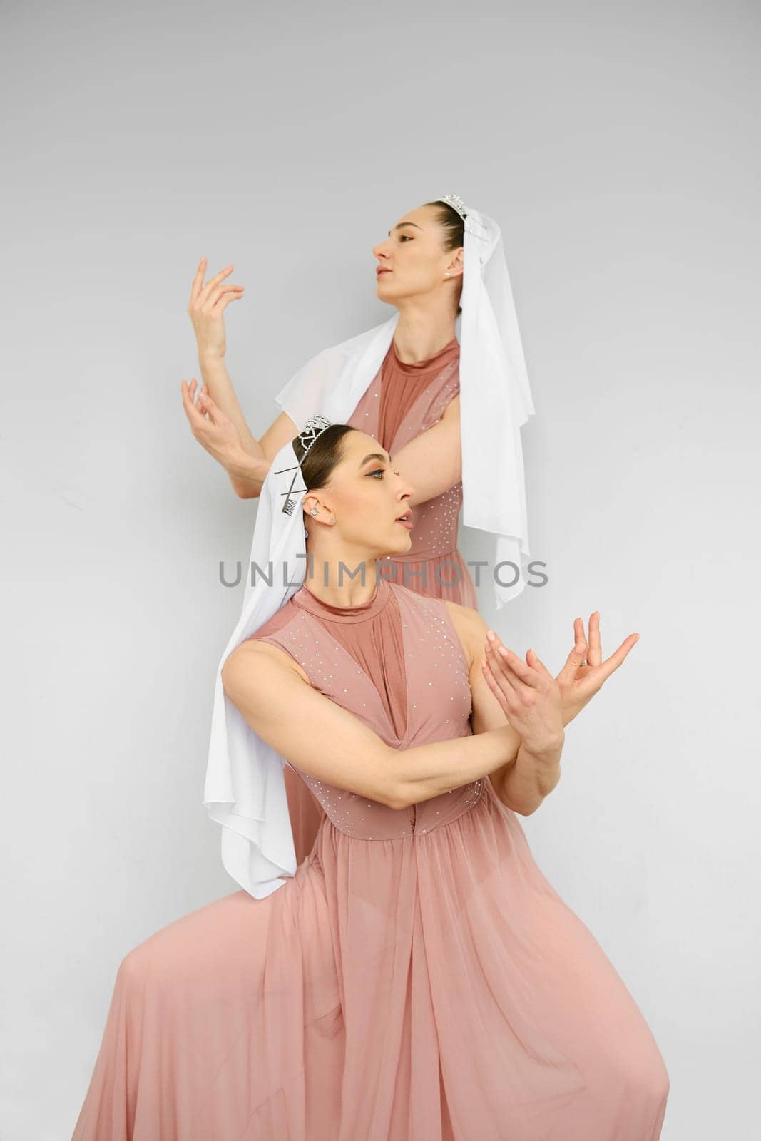 Two female dancers perform hand movements on grey background