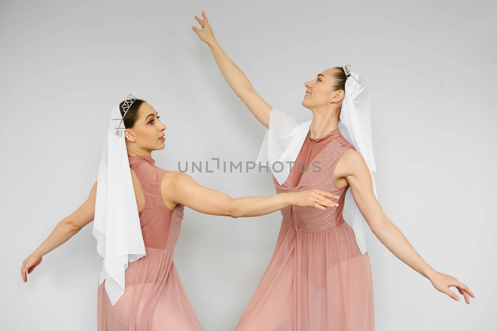 Two ballerinas in peach dress waving hands in front of each other on grey background