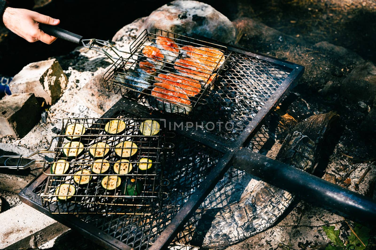 Cooking food on the grill during a picnic in the woods. Salmon steaks and sliced zucchini are grilled over a campfire.