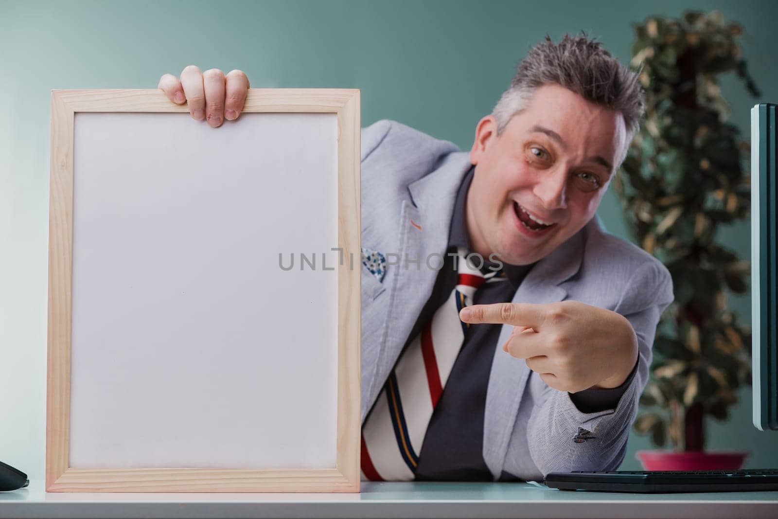 Cheerful businessman in a grey suit playfully points at a blank whiteboard, ready to present fresh ideas