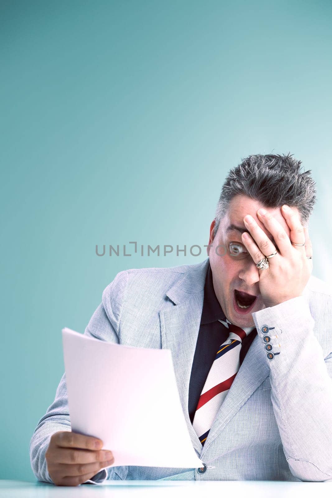 Shocked anchorman in grey suit covers his face, reacting to unbelievable news in the document he holds