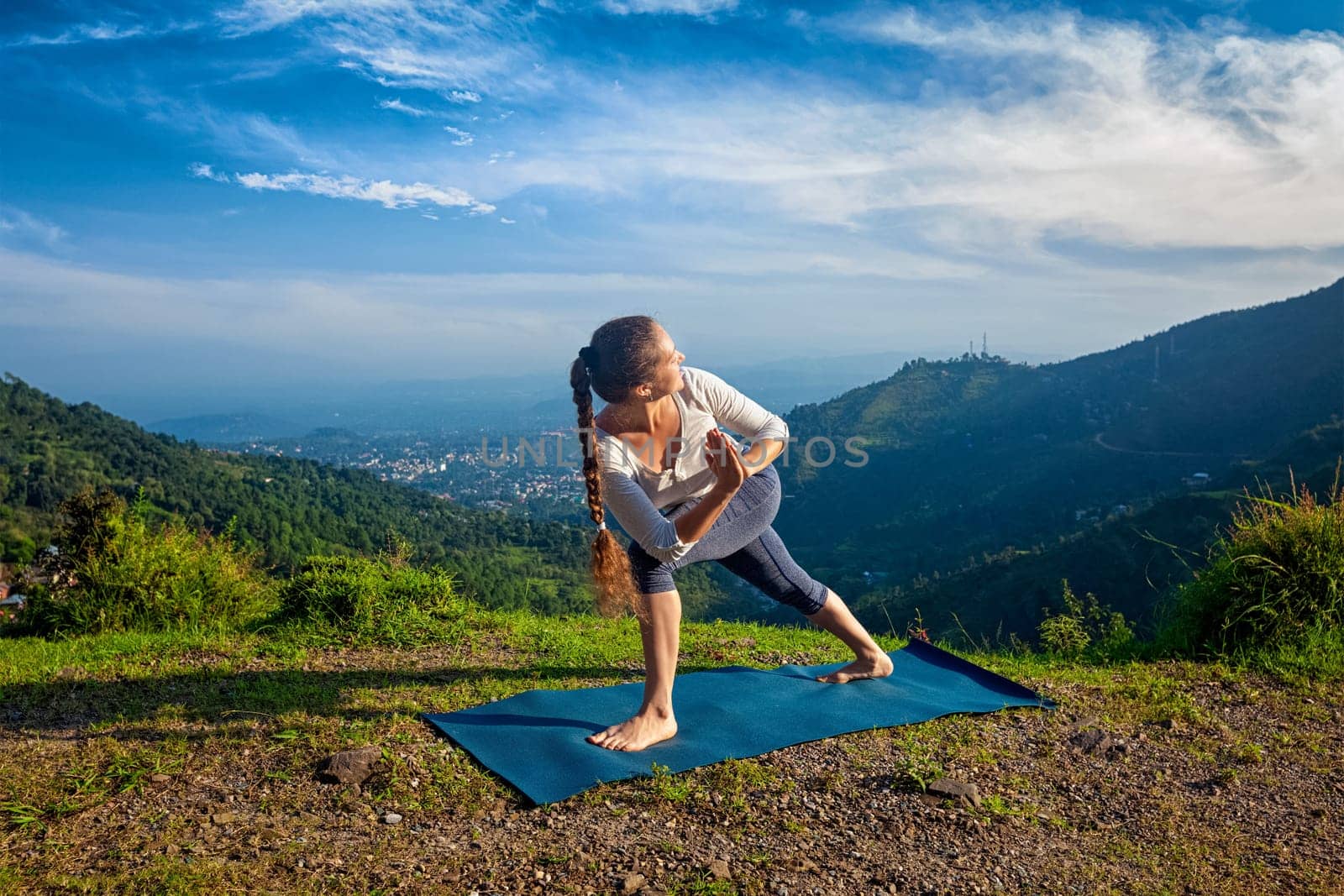 Woman practices Ashtanga Vinyasa yoga asana Utthita Parsvakonasana varitation - extended side angle pose outdoors in mountains in the morning