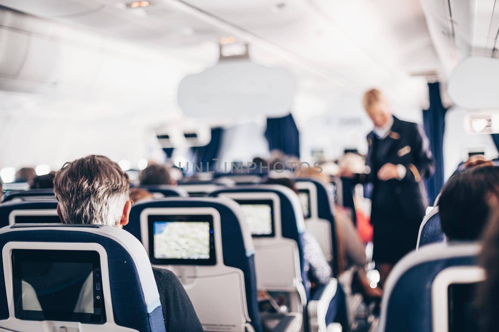 Interior of airplane with passengers on seats and stewardess in uniform walking the aisle, serving people. Commercial economy flight service concept