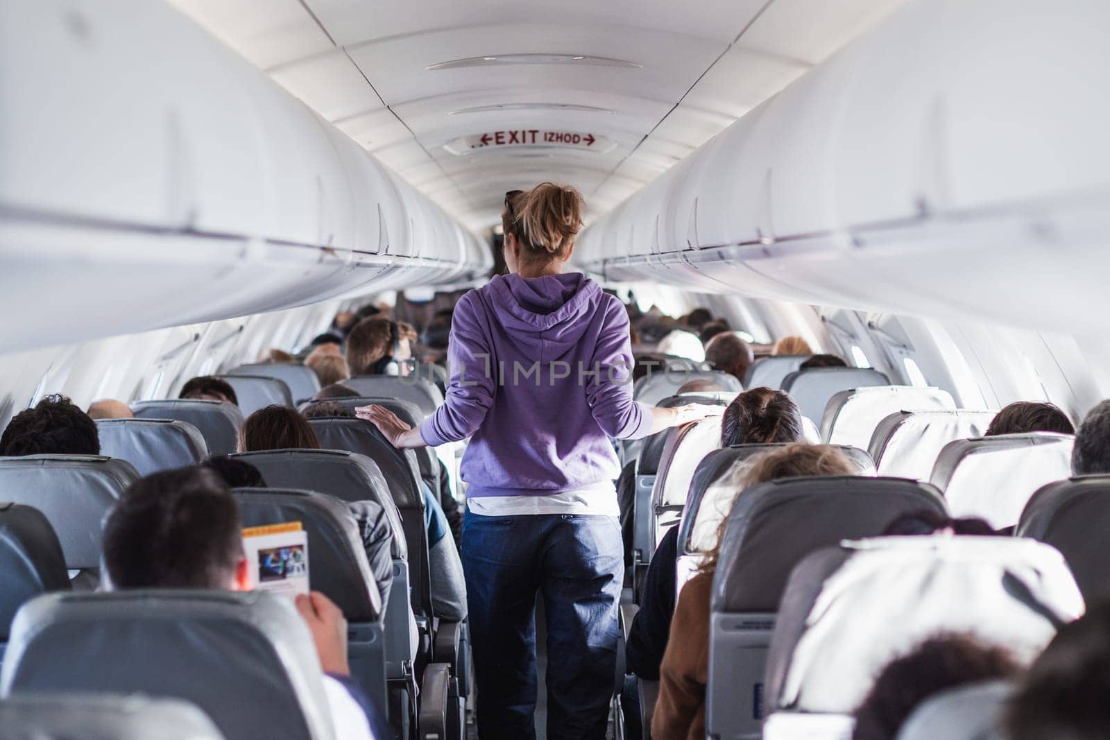Interior of airplane with passengers on seats and female traveler walking the aisle. Commercial economy flight service concept