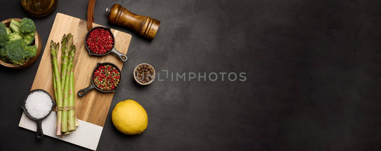 Raw asparagus, broccoli and spices on black background, top view. Copy space