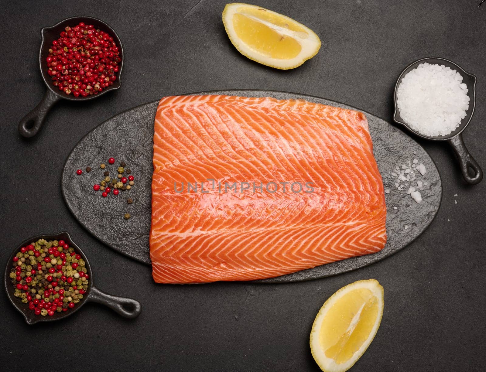 Raw piece of trout on a black board and spices, top view