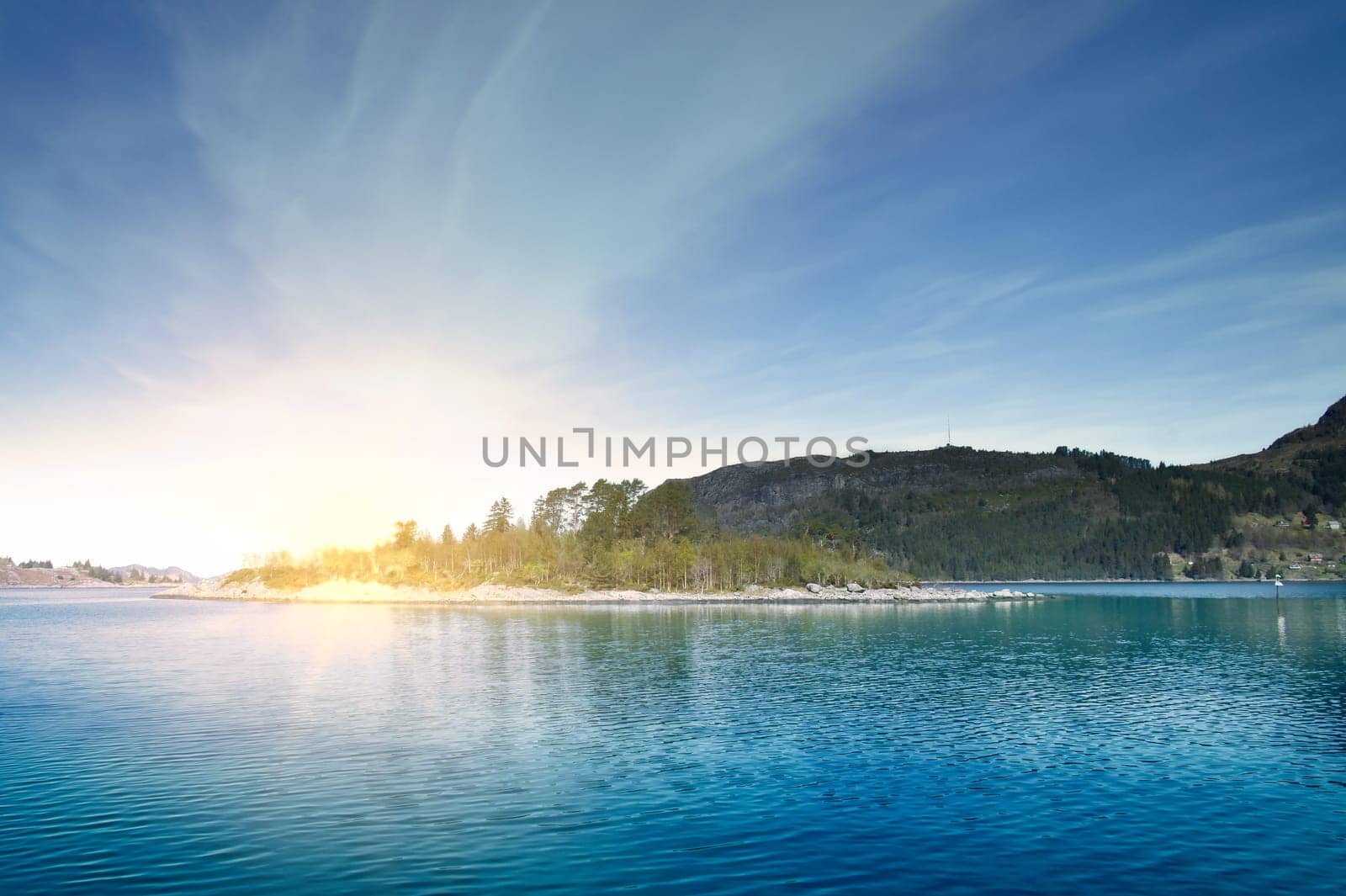 Island with rocks and trees in the fjord in front of the open sea in Norway. The water glistens in the sun. Landscape from the north