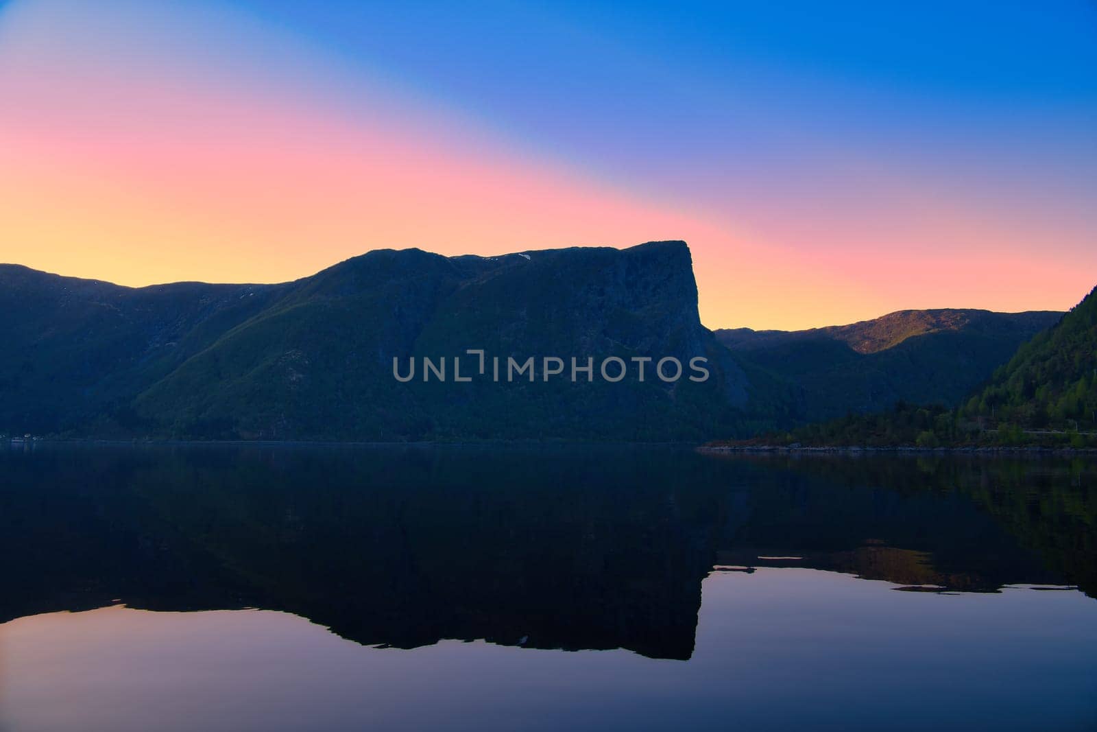 Norwegian fjord landscape at dusk. View of mountains with rough vegetation. Crystal clear water in the foreground. Landscape from Scandinavia