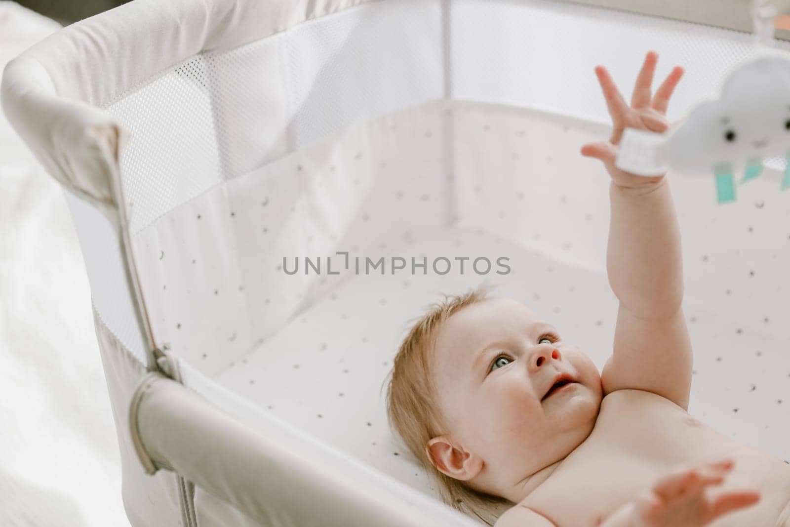 Cute little baby girl lying in the bed crib and playing with hanging mobile toy. Newborn care. Healthy childhood. Smiling infant, child or kid. High quality photo