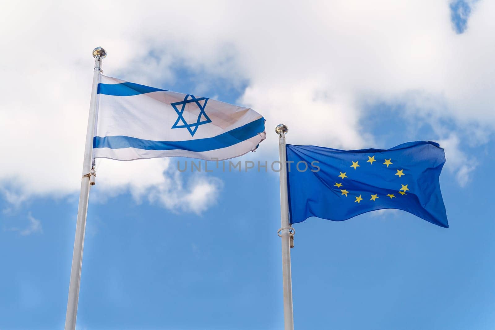 The Israeli flag and the EU flag fly against the sky. Cooperation and mutual support between Israel and the countries of the European Union.