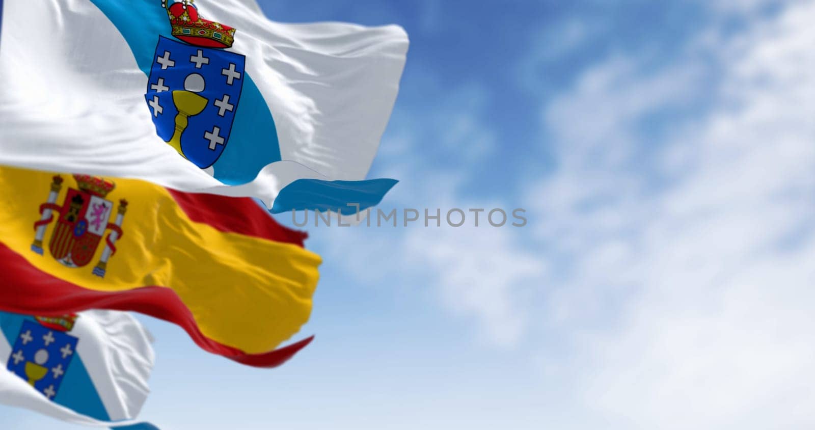 Flags of Galicia and Spain waving on a clear day. Autonomous community of Spain. White with a blue diagonal band with coat of arms on top. 3d illustration render. Selective focus. Fluttering fabric