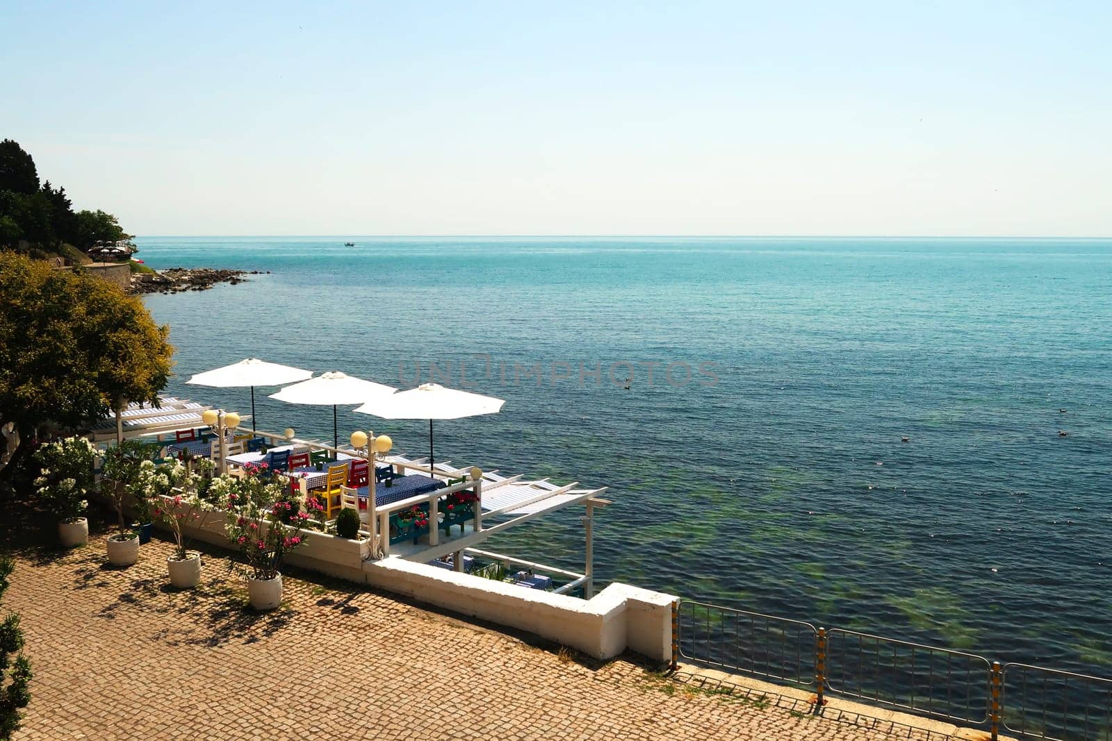 Picturesque view onto the deep blue sea from the old town of Nessebar, Nesebar with a restaurant terrace in the foreground with colorful chairs, table cloths and white umbrellas, Bulgaria 2022