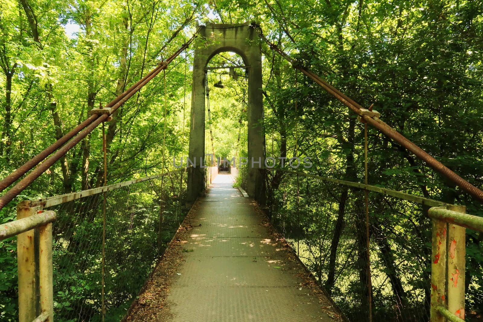 Entering the Mavrikov Rope Bridge, a small metal pedestrian suspension bridge over the Yantra River in a lush and dense forest around Veliko Tarnovo, Bulgaria 2022