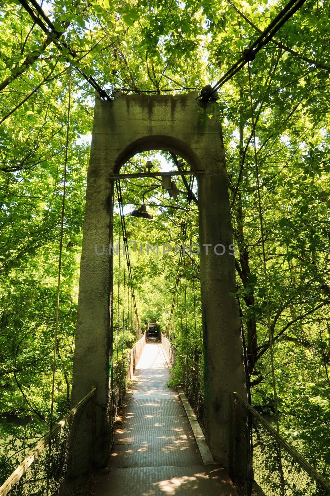 Entering the Mavrikov Rope Bridge, a small metal pedestrian suspension bridge over the Yantra River in the dense lush forest around Veliko Tarnovo, Bulgaria 2022