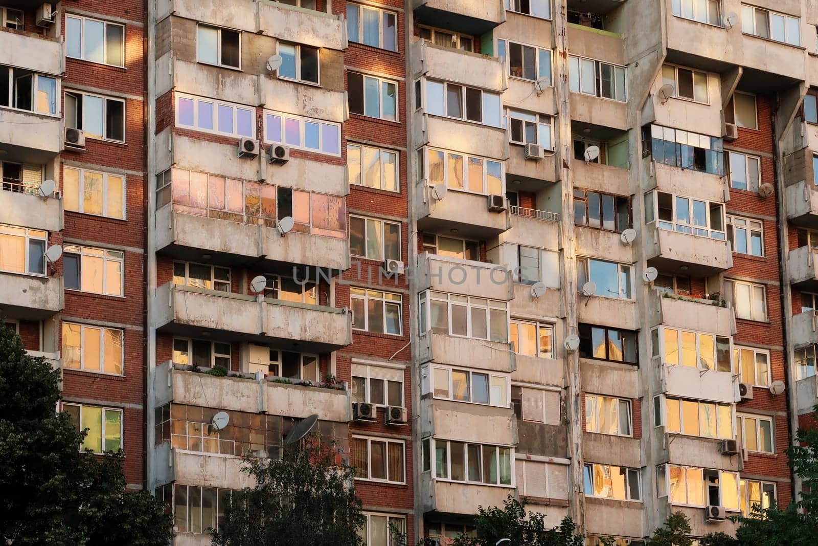The sunset reflecting in the many windows of a concrete, socialist, brutalist panel, multi-story, high-rise, apartment block, building, orange, yellow, pink reflection, Sofia, Bulgaria 2022