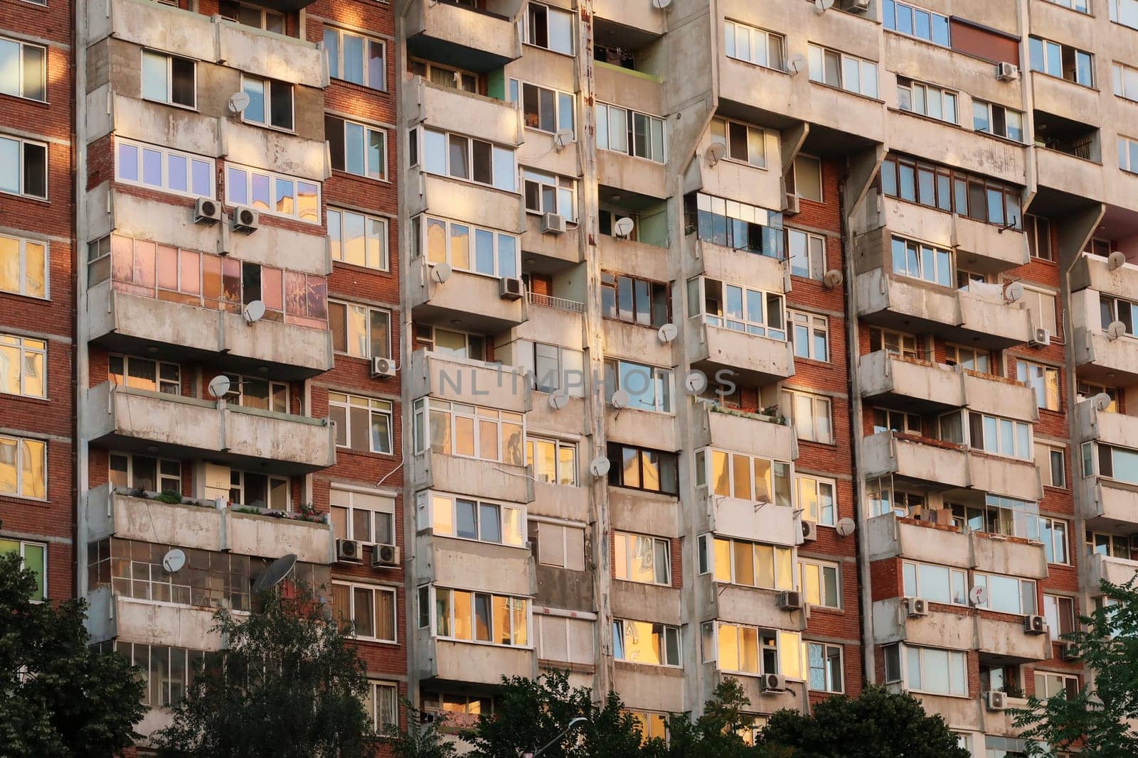 The many windows of a concrete, socialist, brutalist panel, multi-story, high-rise, apartment block, building are reflecting the sunset in orange, yellow, pink color, Sofia, Bulgaria 2022
