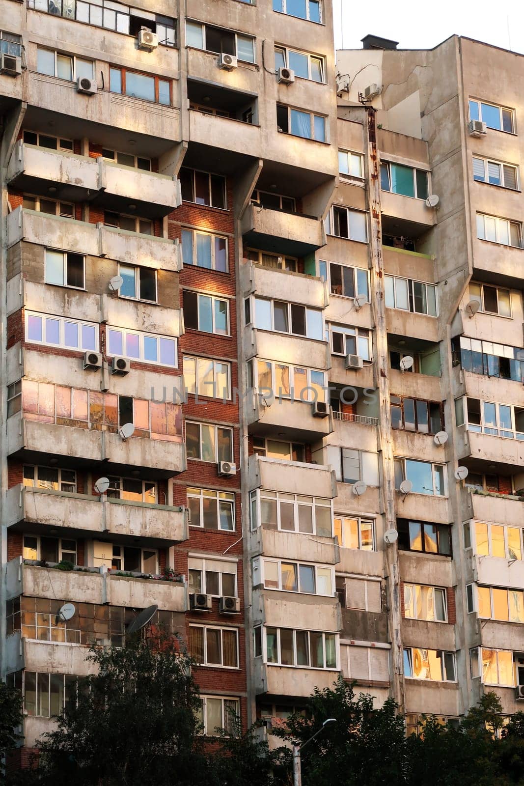 The sunset reflecting in orange, yellow, pink in the many windows of a concrete, socialist, brutalist panel, multi-story, high-rise, apartment block, building, Sofia, Bulgaria 2022