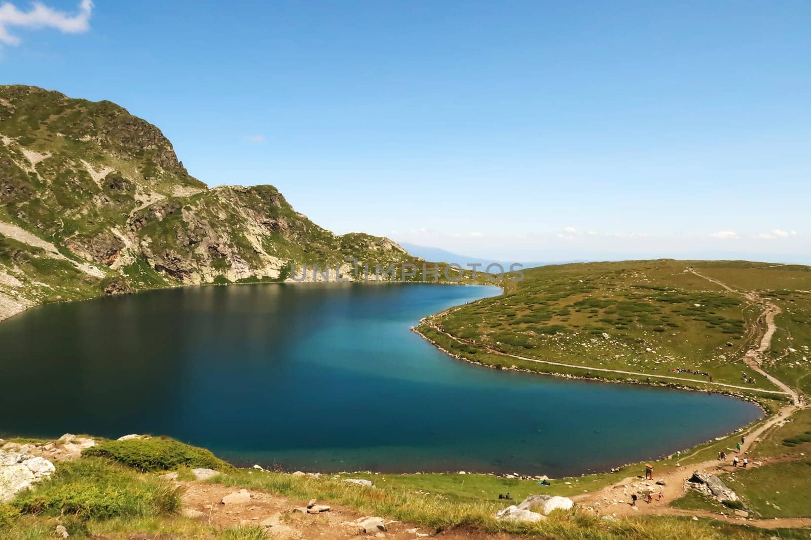Spectacular view onto the deep blue Kidney, Babreka Lake, one of the Seven Rila Lakes, situated on a plateau in the Rila National Park, a few people are on the hiking trail right next to it, close to Sofia, Bulgaria 2022