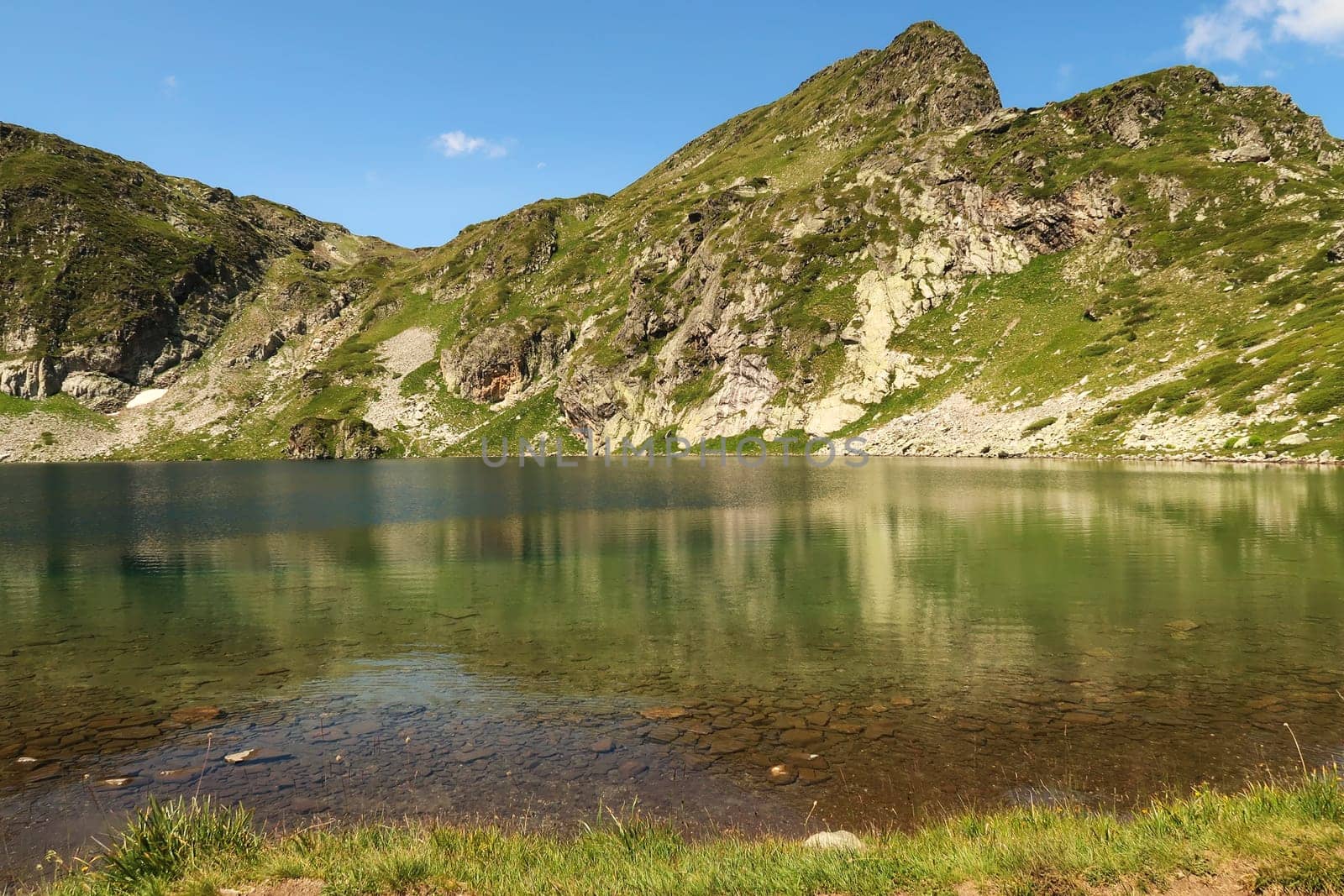 The mountains are reflecting on green, blue and turquoise water of the Kidney, Babreka Lake, one of the Seven Rila Lakes, situated on a plateau in the Rila National Park, close to Sofia, Bulgaria 2022