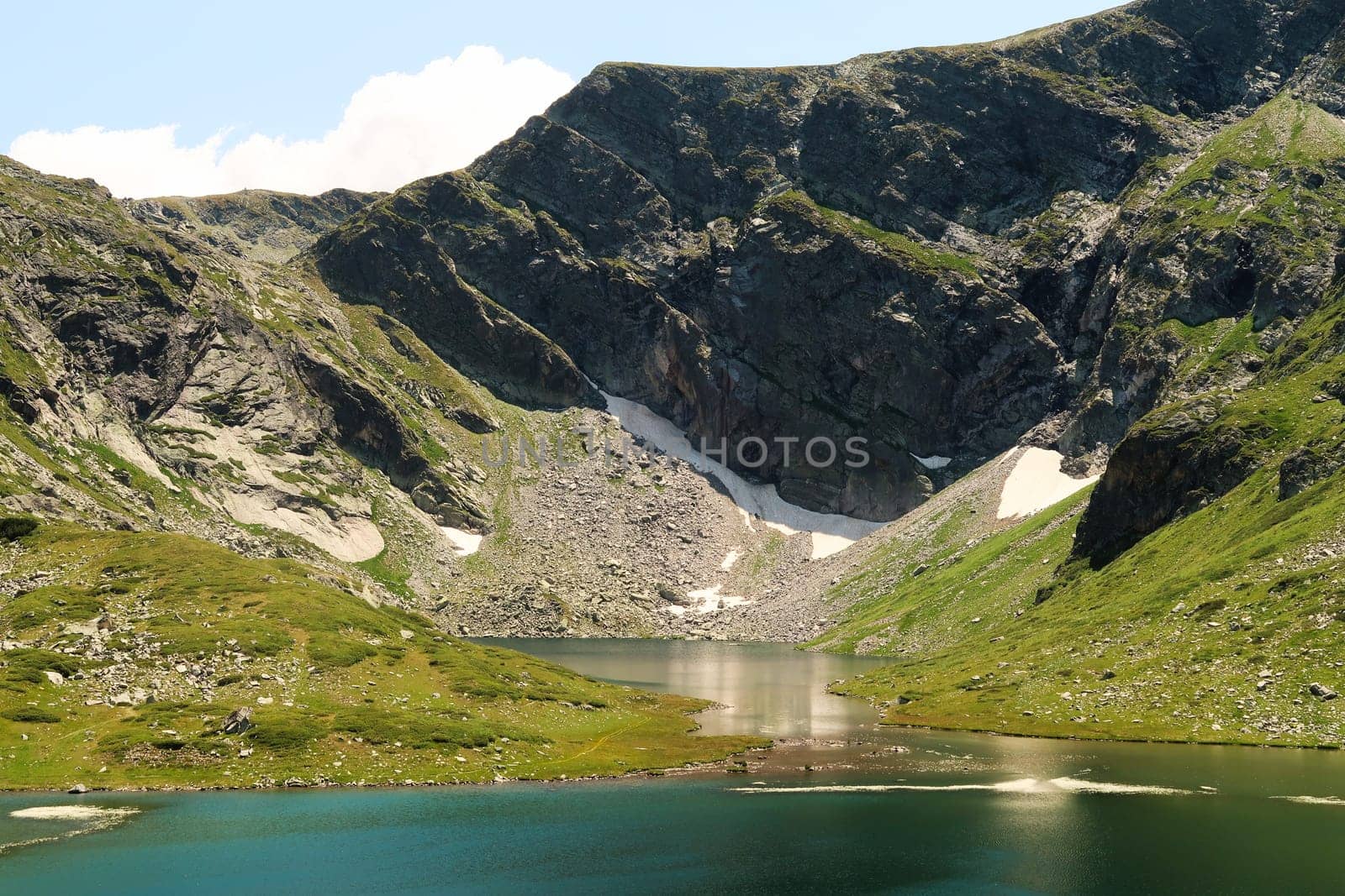 The mountains are reflecting on green, blue and turquoise water of the Fish Lake, Ribnoto Ezero, one of the Seven Rila Lakes, situated on a plateau in the Rila National Park, close to Sofia, Bulgaria 2022
