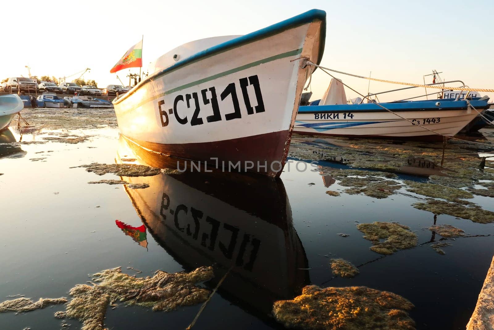 A fisherboat with the bulgarian flag perfectly reflecting in the water at the harbor, port next to the old town of Sozopol, Sosopol, Bulgaria, 4th of July 2022
