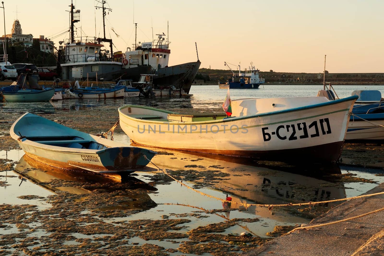 Small fisherboats reflecting in the water at the golden hour in the harbor, port next to the old town of Sozopol, Sosopol, Bulgaria, 4th of July 2022