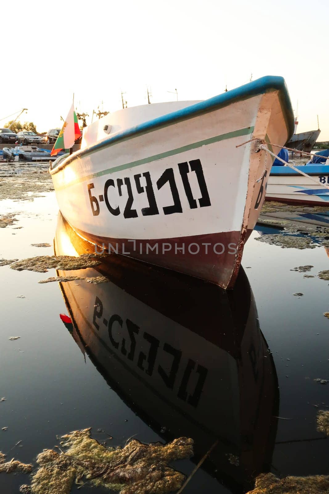 A fisherboat with the bulgarian flag reflecting perfectly in the water at the harbor, port next to the old town of Sozopol, Sosopol, Bulgaria, 4th of July 2022