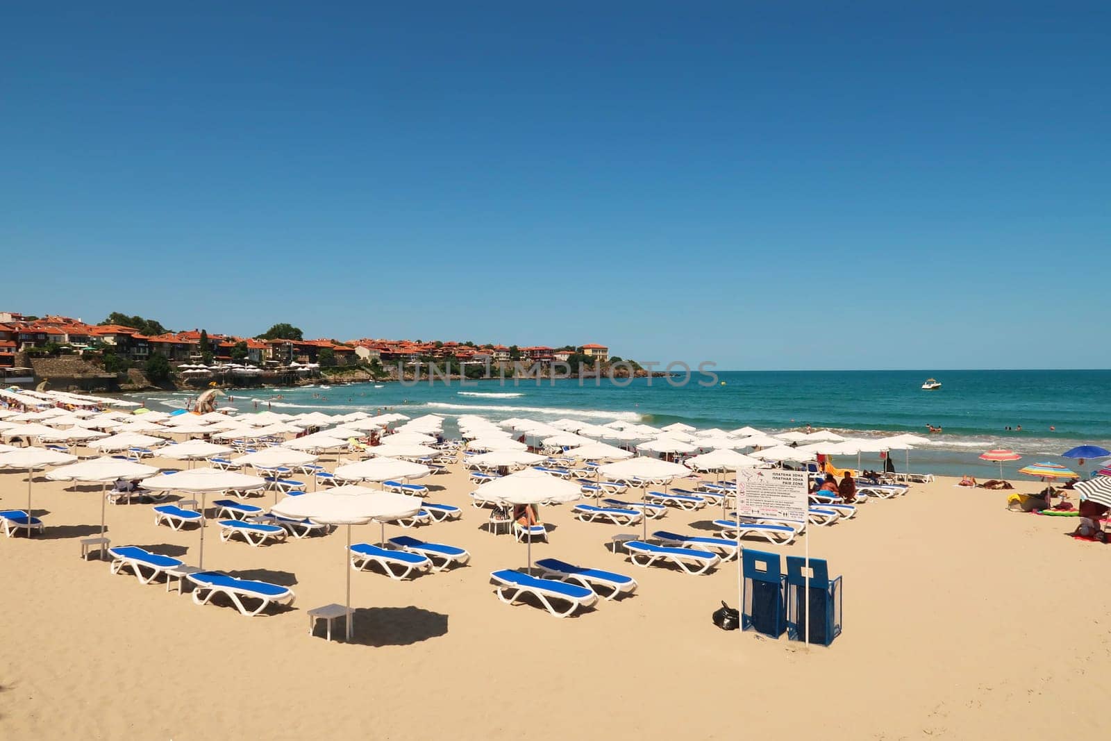 The Sozopol Central Beach, many white beach umbrellas and sun chairs in the foreground and the sea and the old town of Sozopol, Sosopol in the background, Bulgaria, 5th of July 2022