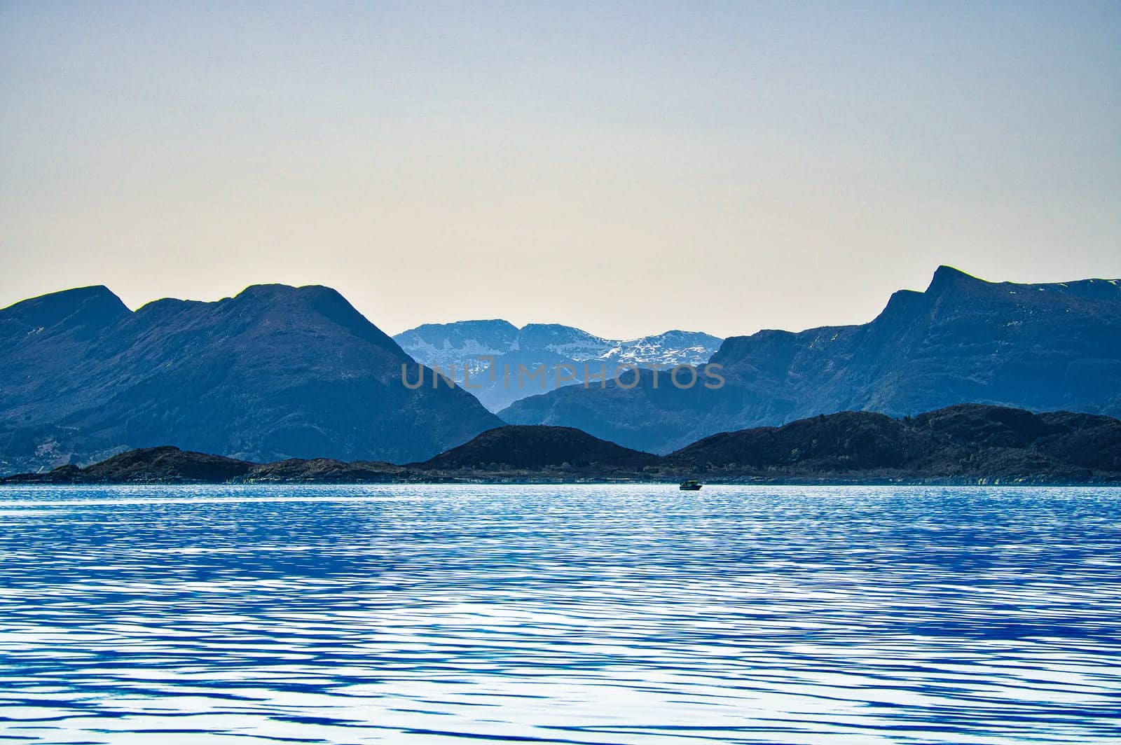 Norwegian fjord landscape. View of snow-capped mountains with rugged vegetation. Crystal clear water in the foreground. Landscape from Scandinavia