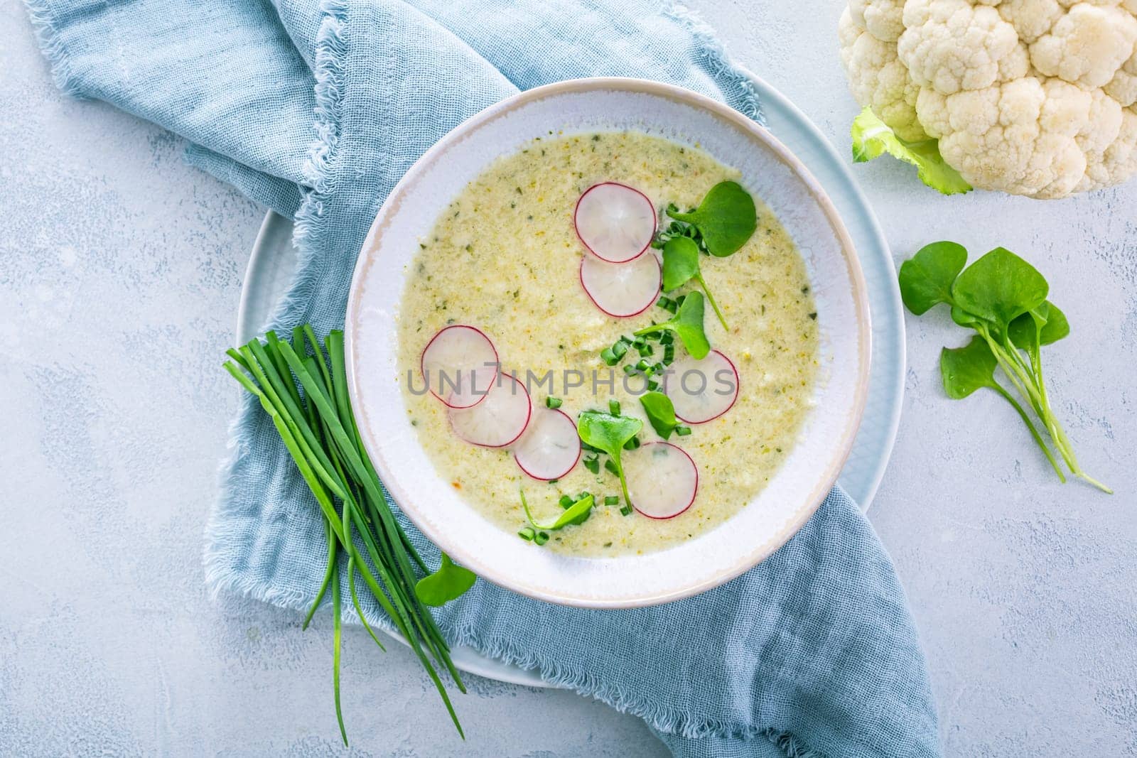 Creamy white cauliflower soup with radish and chives, healthy food with herbs