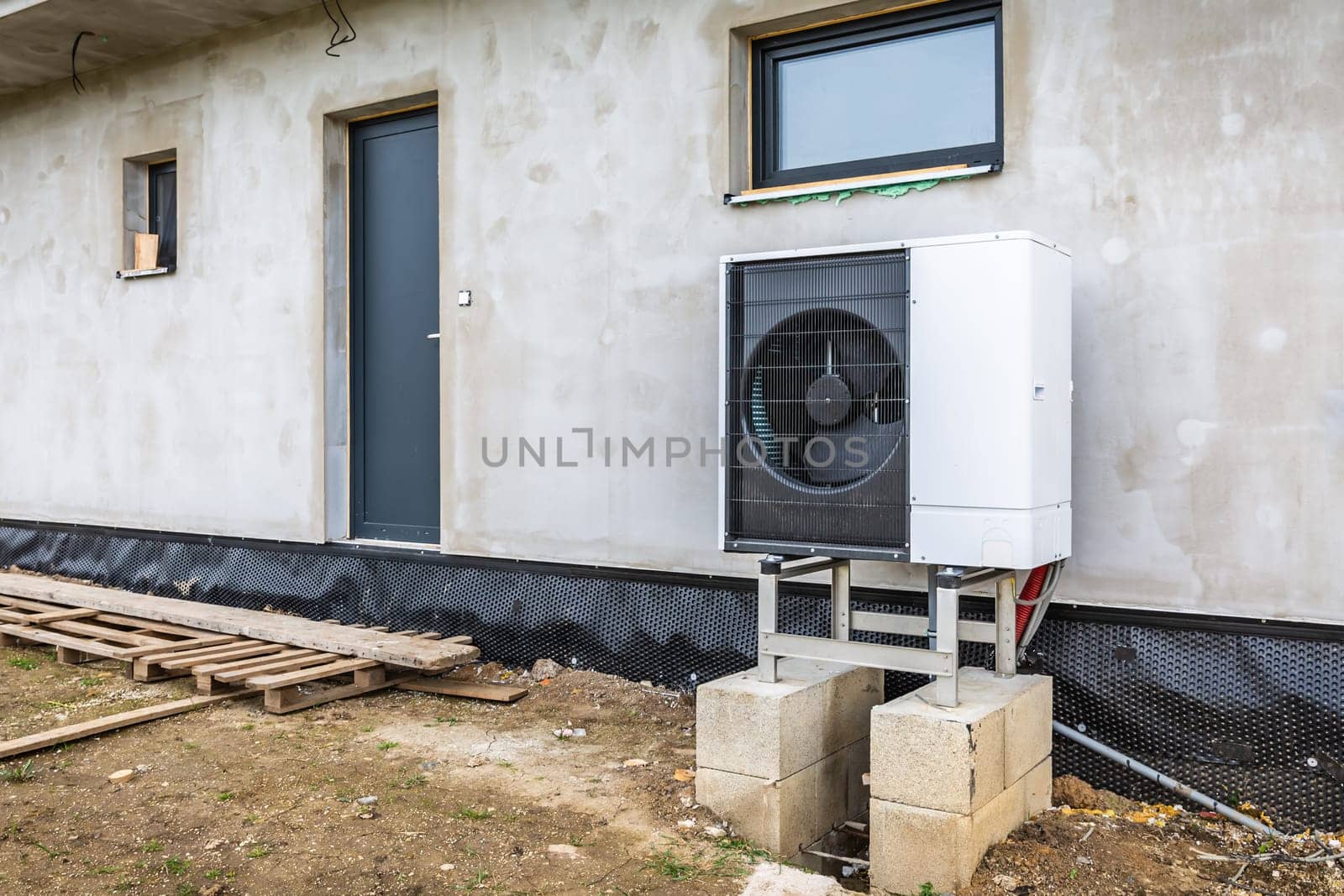 Air source heat pump installed outside of new and modern house under construction, green renewable energy concept of heat pump