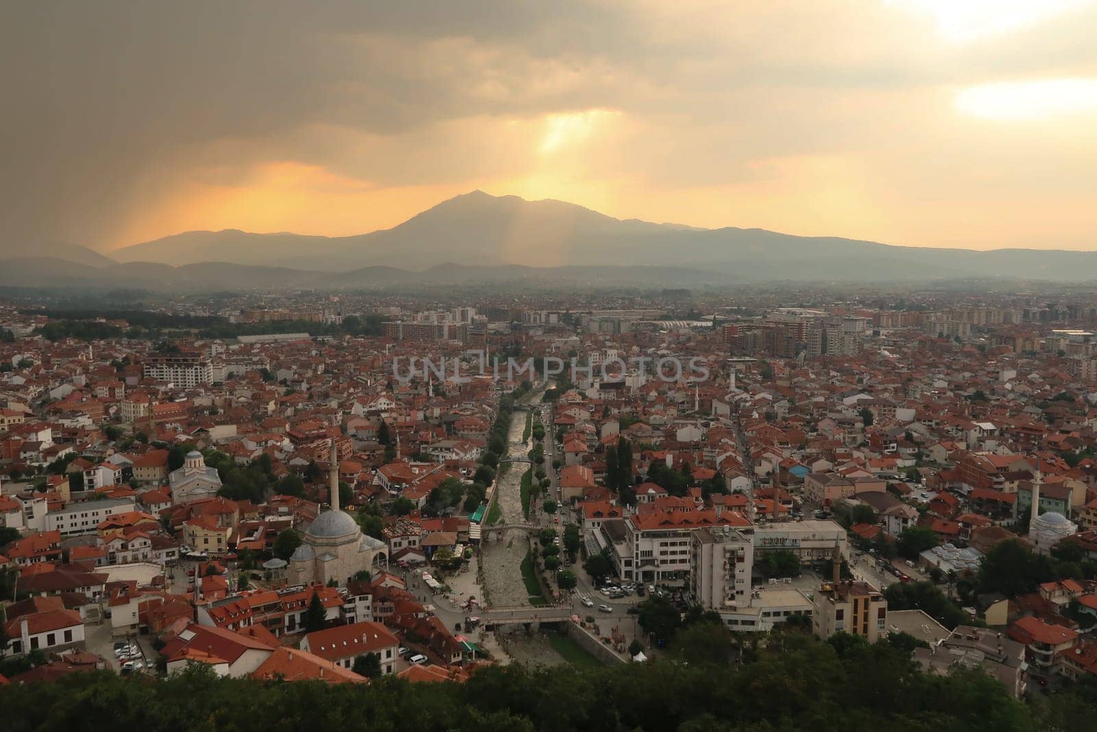 View from the Prizren Fortress onto the old town of Prizren before sunset, golden sunlight breaking through a cloudy sky, Prizren, Kosovo 2022