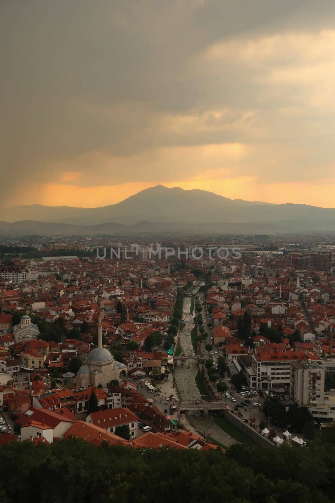 View from the Prizren Fortress onto the Bistrica River and the old town of Prizren before sunset, golden sunlight and a cloudy sky, Prizren, Kosovo 2022