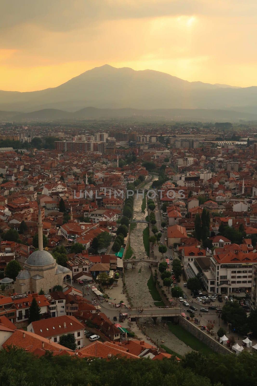 View from the Prizren Fortress onto the Bistrica River and the old town of Prizren before sunset, golden sunlight is breaking through a cloudy sky, Prizren, Kosovo 2022
